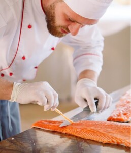 A Chef Dressed in White is Filetating a Big Piece of Salmon