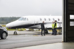 View from the hangar at the Access Oslo VIP terminal in Torp. Three man are standing outside next to a small white jet, talking.
