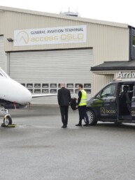 A small jet and a limo from Access Oslo is parked outside the FBO VIP lounge. Two men are walking towards the hangar.