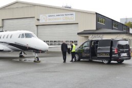 A small jet and a limo from Access Oslo is parked outside the FBO VIP lounge. Two men are walking towards the hangar.