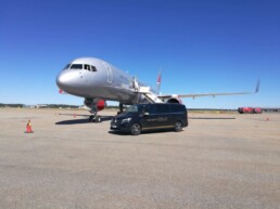 Gray plane is parked and a short limousine is standing outside.