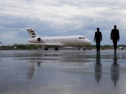 Two people walking towards a white plane that is parked on a wet runway