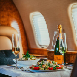 Cesar salad on two plates inside a private jet. Warm atmosphere. Two glasses with Veuve Cliquot and a bottle in the background