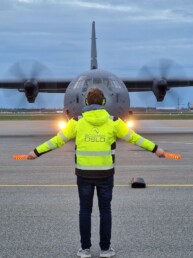 A man in a yellow jacket is handling a military, gray airplane in Oslo